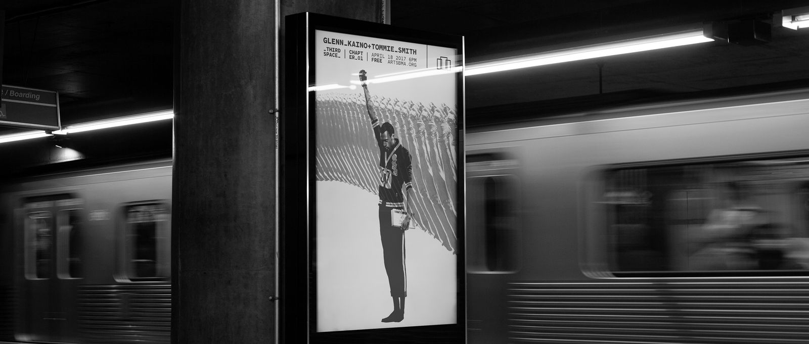 black and white image of poster display in a subway station, train streaking by in motion