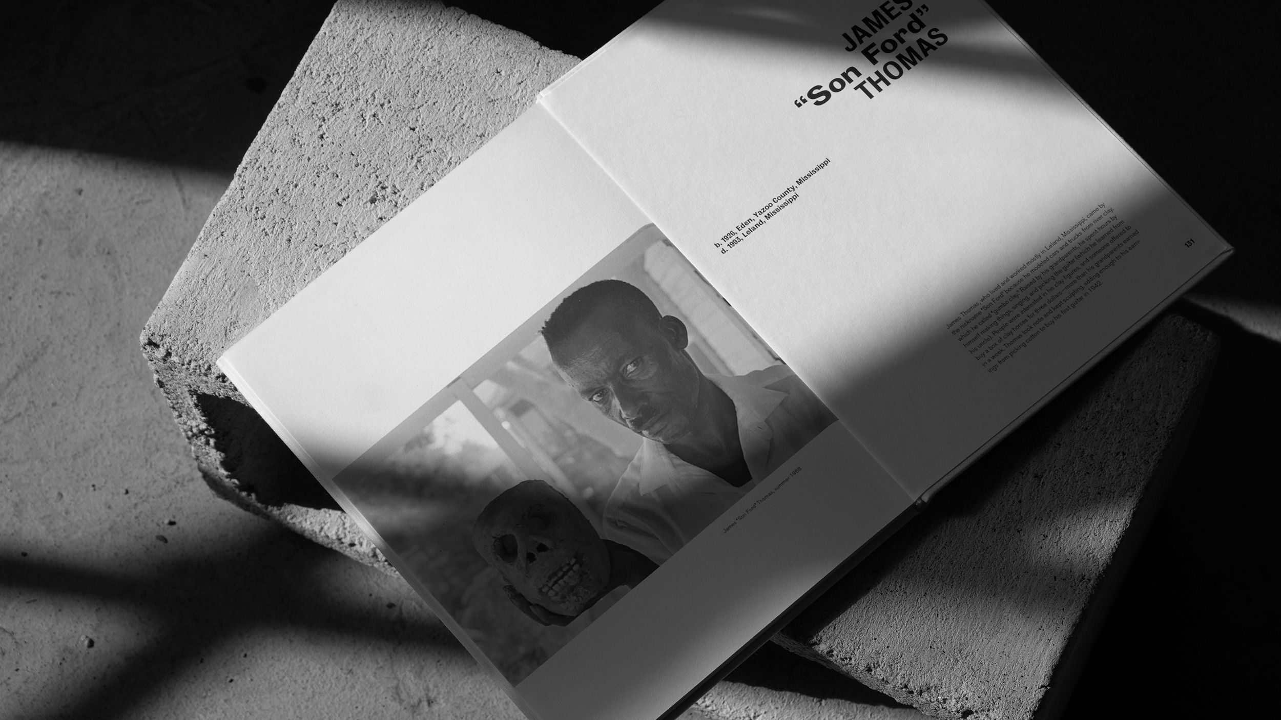 black and white image of an open book sitting on a concrete block in harsh light and shadows